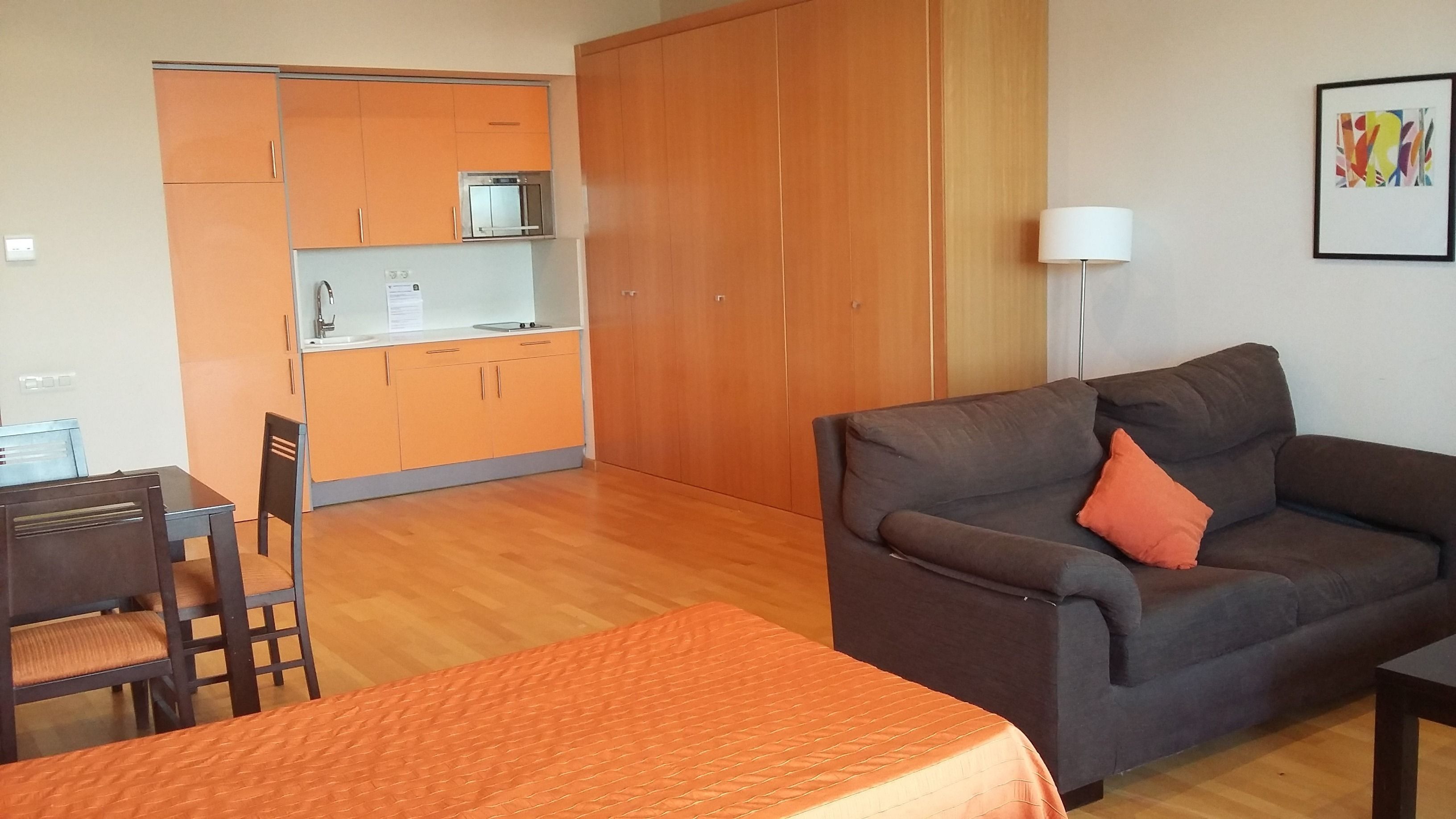 A compact living space with a kitchenette, a sofa, a dining table, and a bed.
