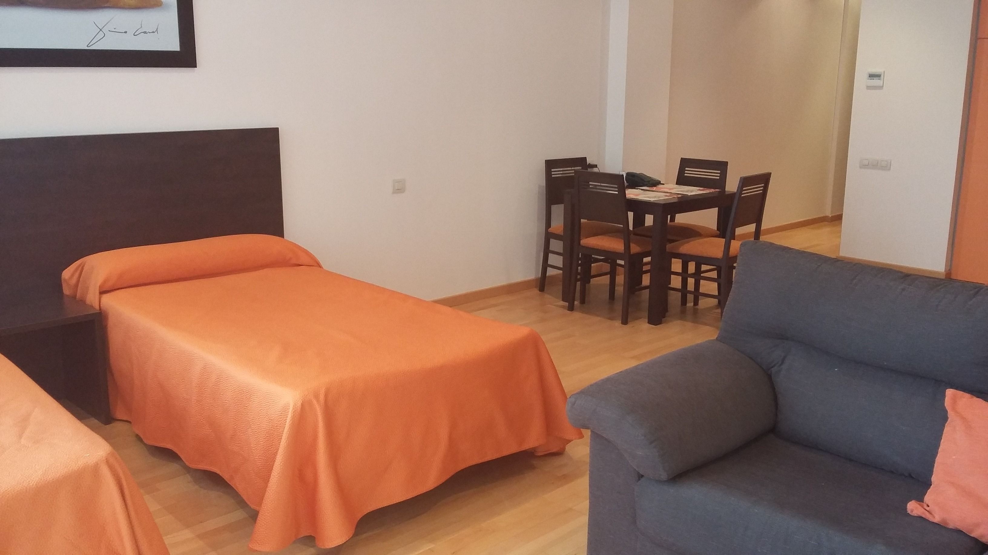Une petite pièce meublée, comprenant un lit, un canapé, une table à manger avec des chaises et un interrupteur fixé au mur.
