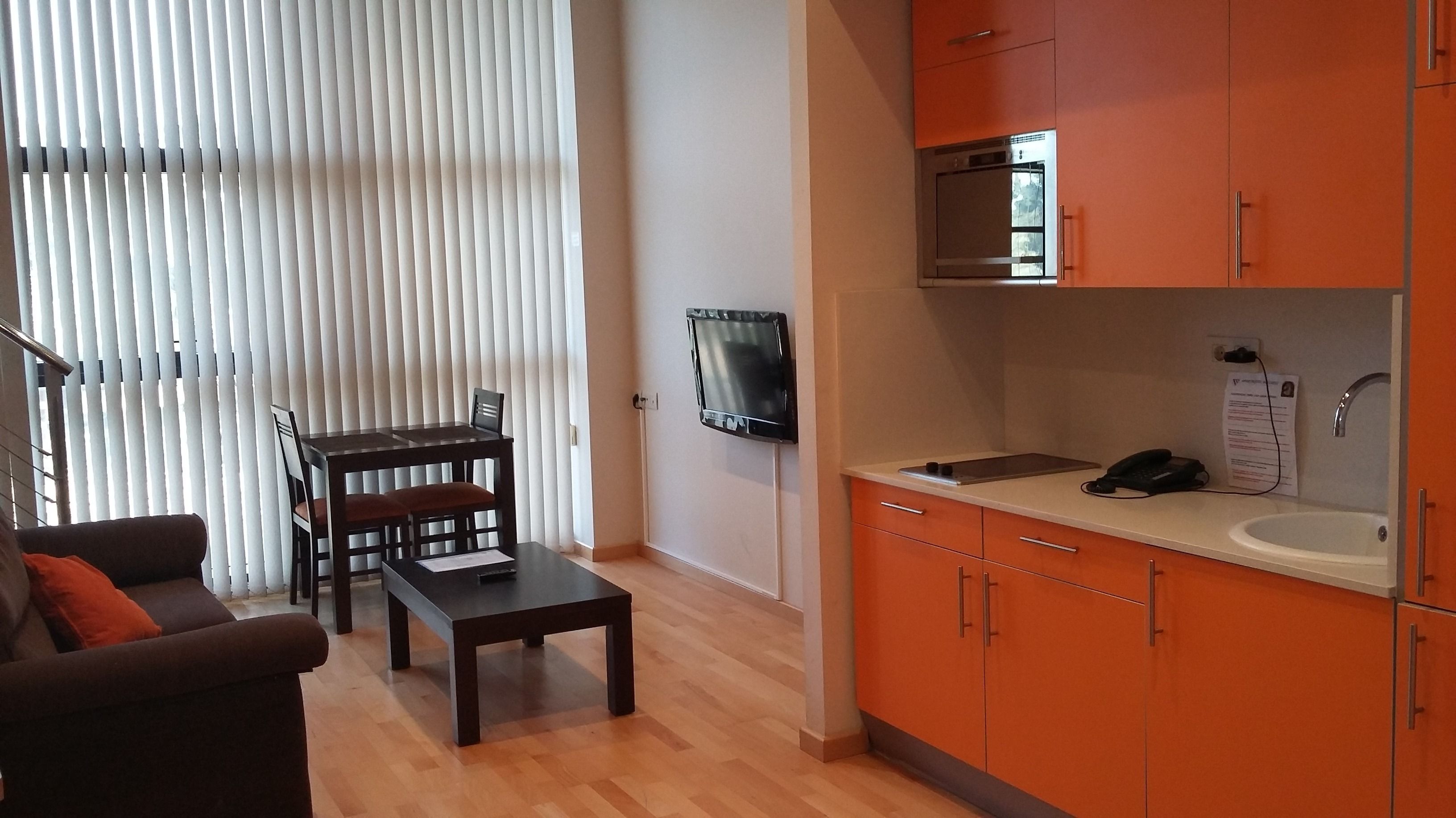 Un espacio habitable compacto con comedor, kitchenette y zona de estar con sofá y mesa.