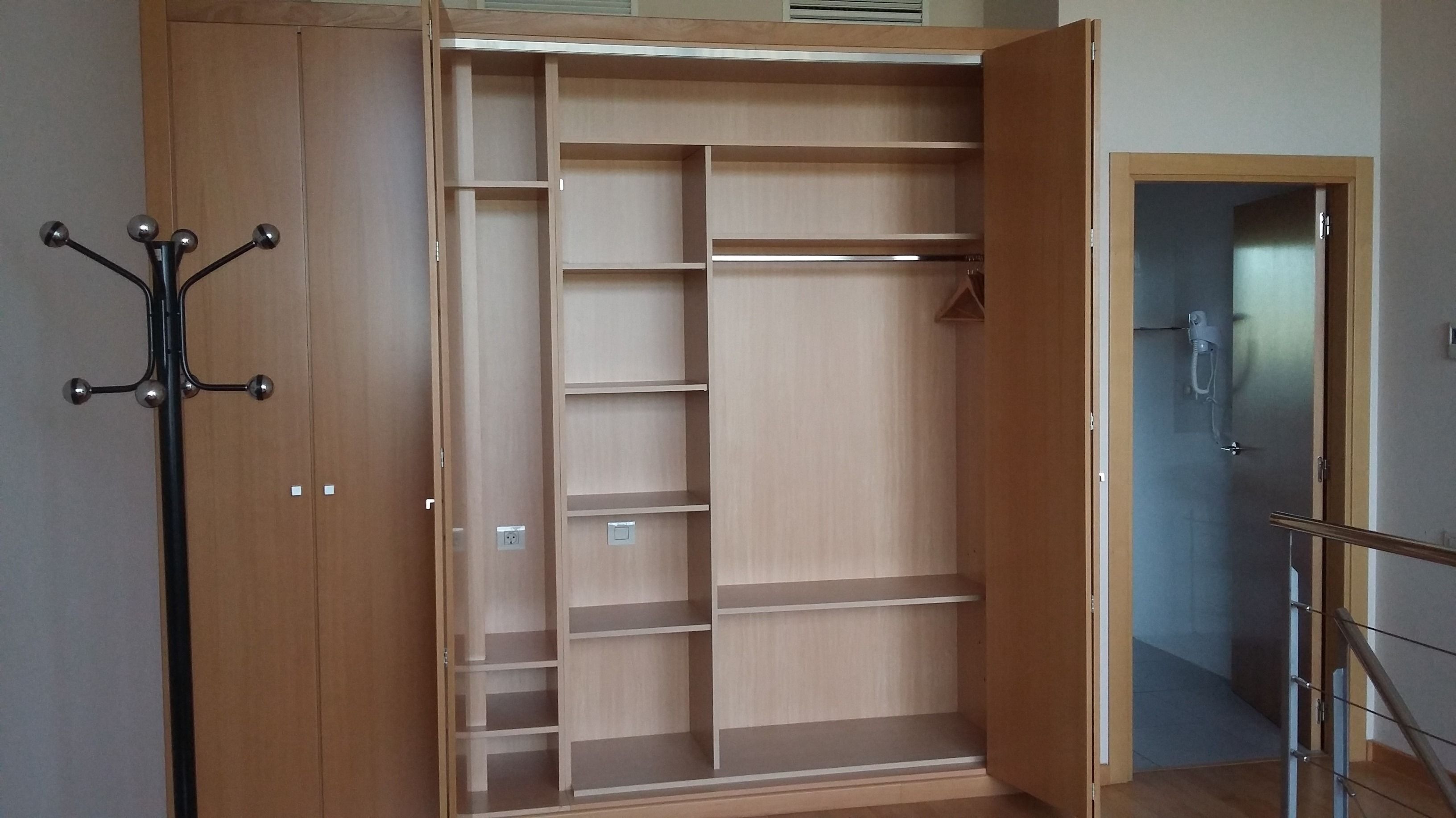 A walk-in closet with multiple shelves and hanging space, a coat rack, and a door leading to another room.