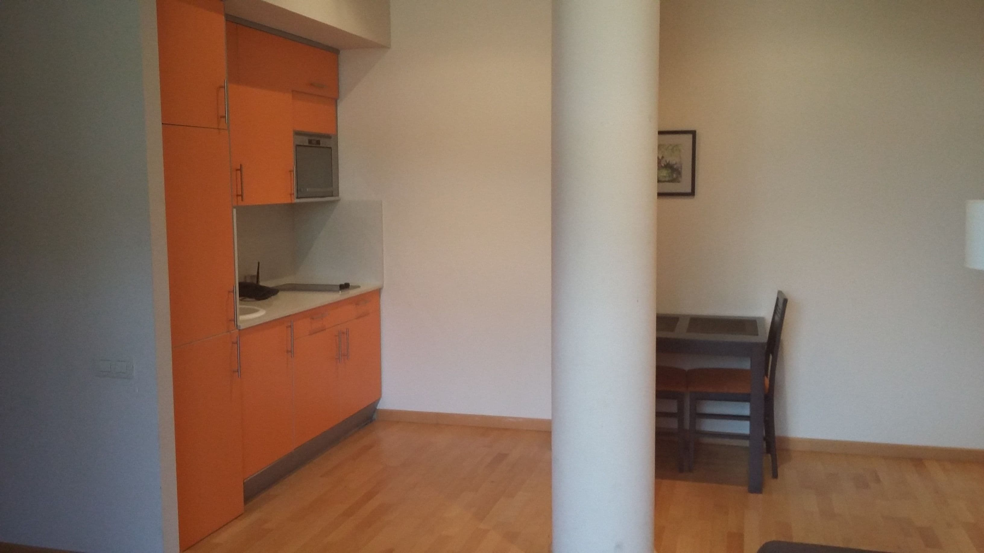 Une cuisine avec des meubles de couleur orange, un plan de travail blanc et une table à manger en bois avec des chaises.