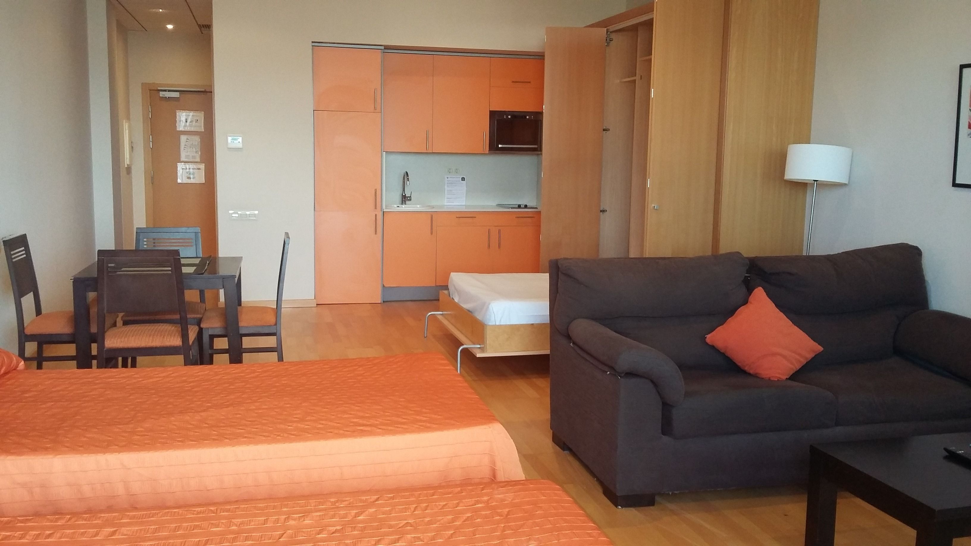 A hotel room with a sofa, a bed, a desk with chairs, and a kitchenette.