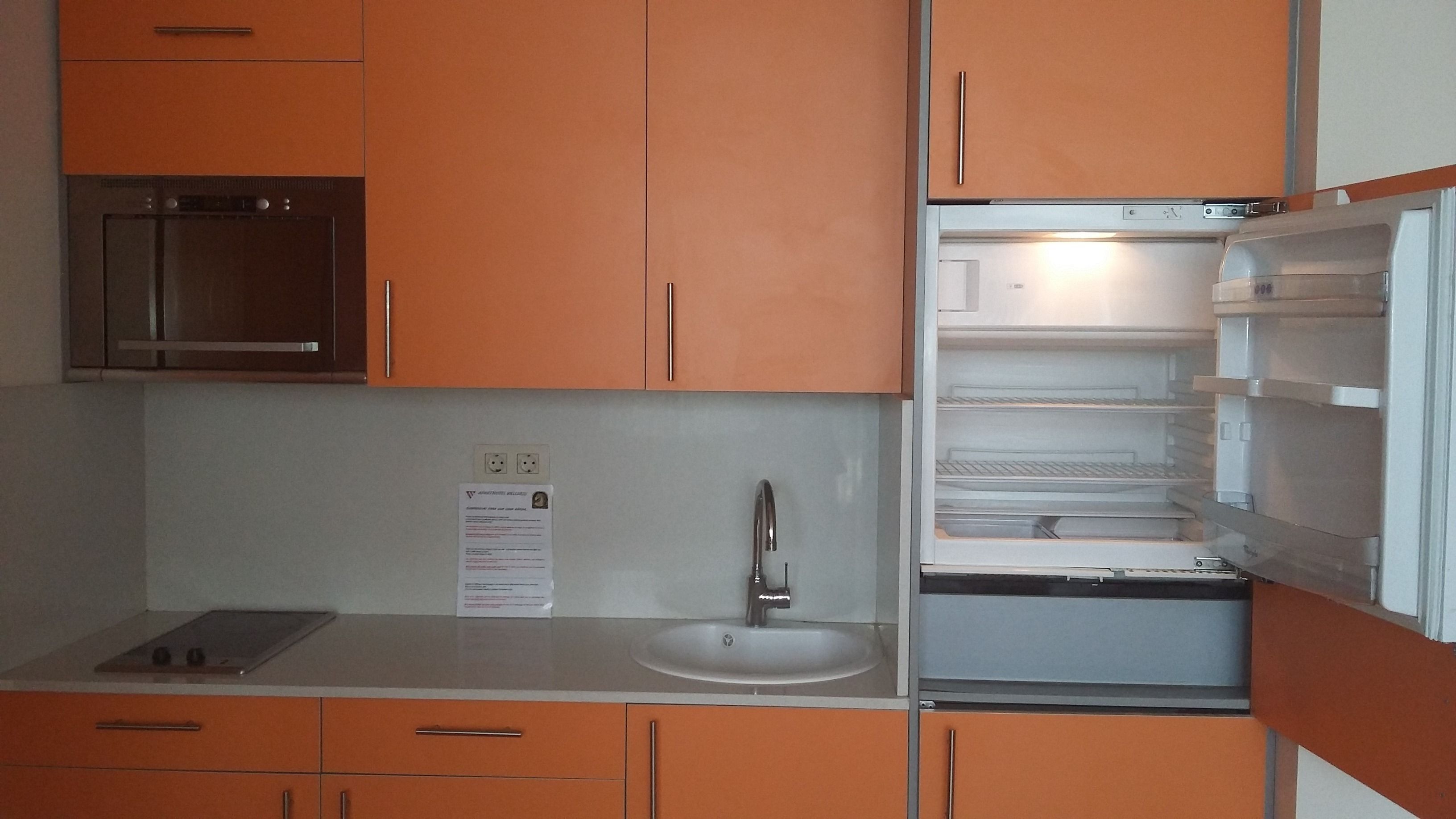 A kitchen with orange cabinets, a stainless steel microwave, a sink, and a refrigerator.