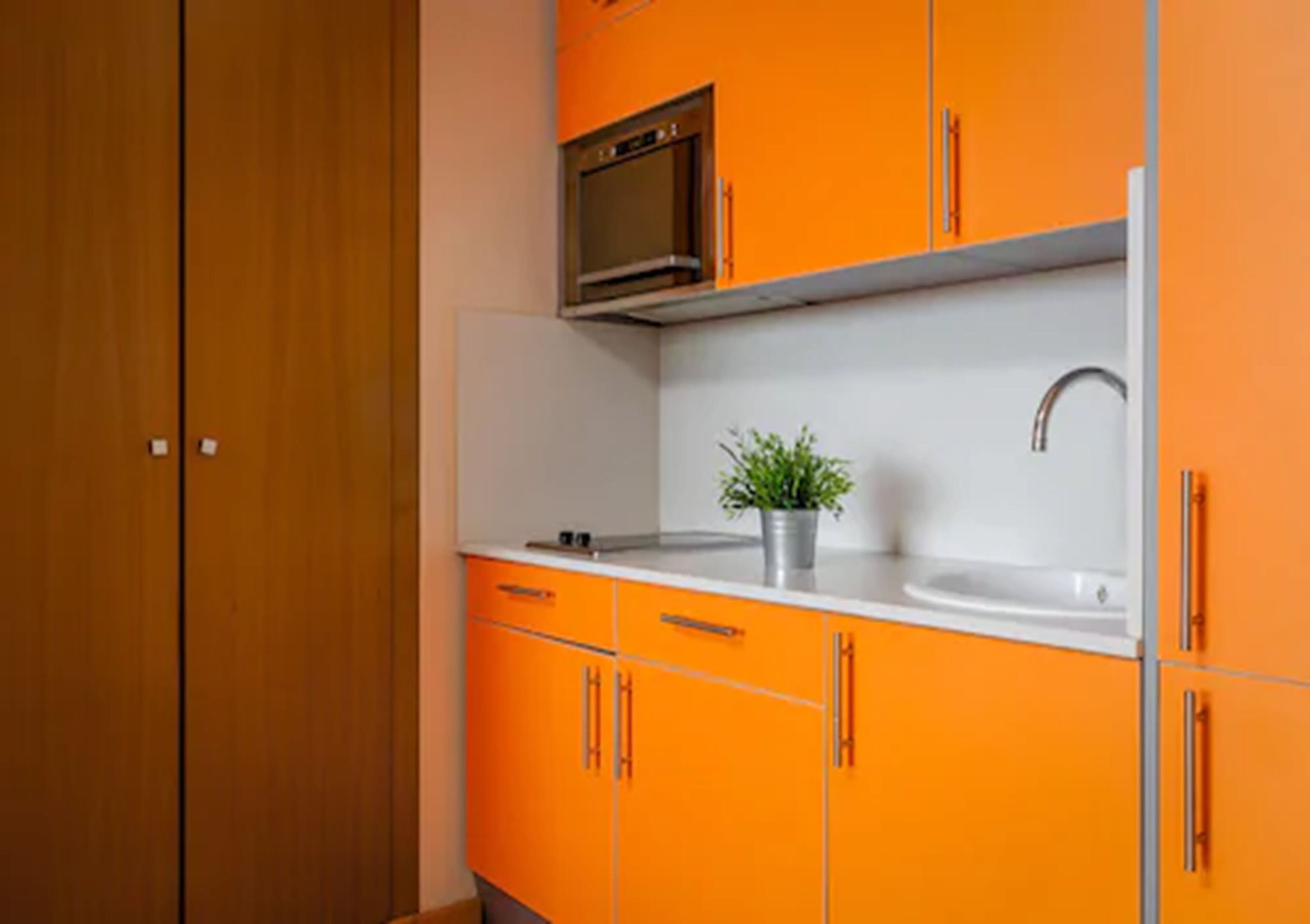 Een kleine keuken met oranje kastjes, een wit aanrecht, een spoelbak en een magnetron.