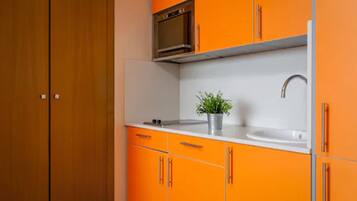Een kleine keuken met oranje kastjes, een wit aanrecht, een spoelbak en een magnetron.