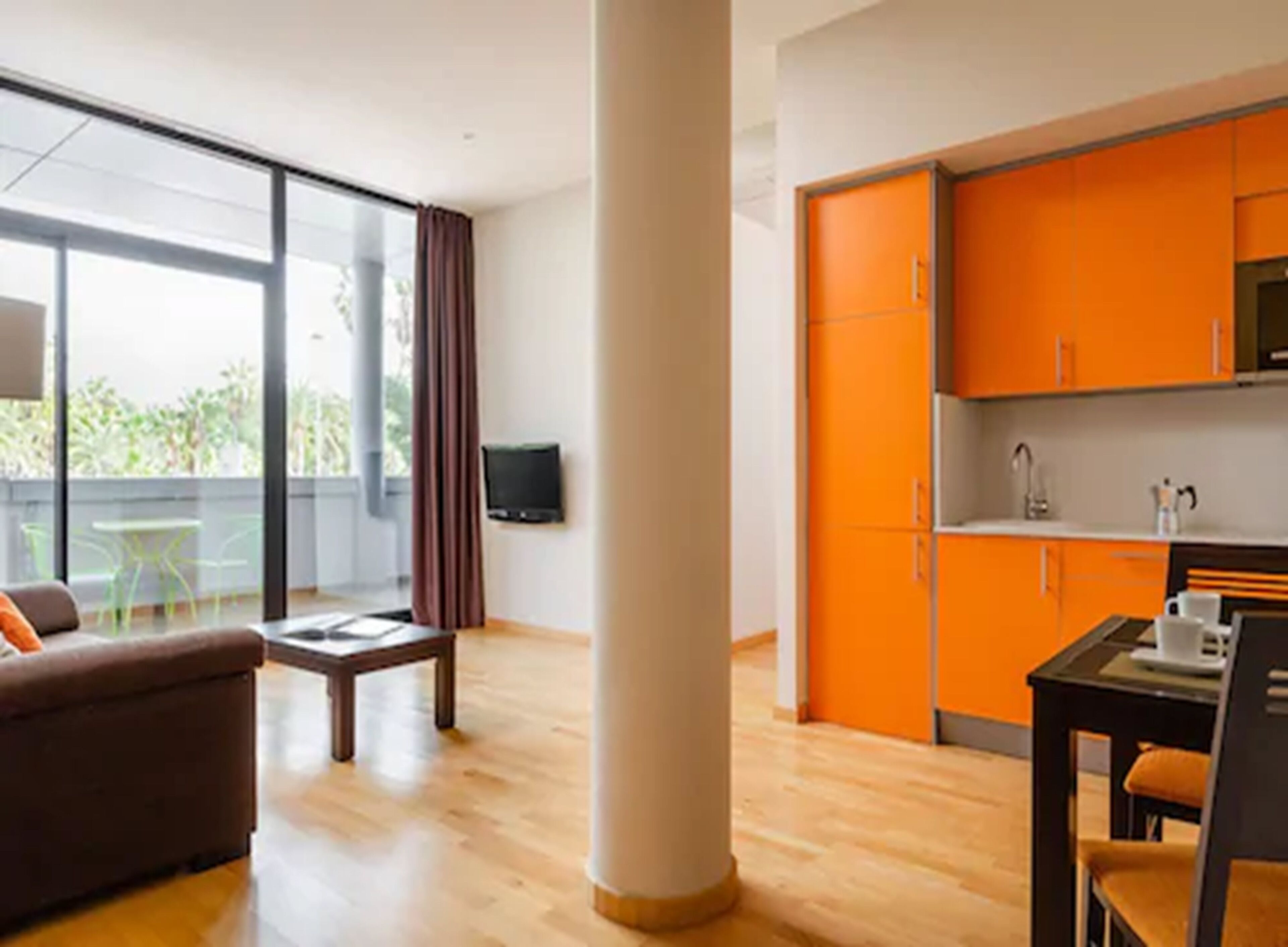 Ein modernes Wohnzimmer mit einer Couch, einem Couchtisch und einem Essbereich mit Tisch und Stühlen. Ein großes Fenster mit Vorhängen, ein flachbildfernseher an der Wand und eine orangefarbene Küche mit Schränken und einer Spüle.