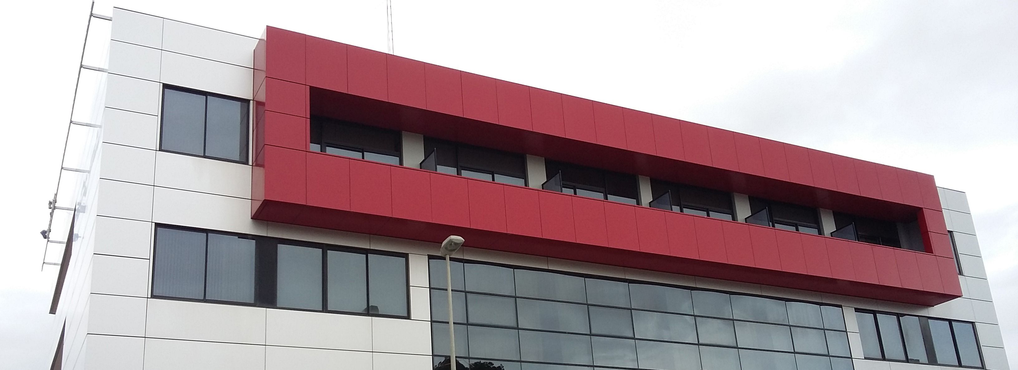 Ein modernes Gebäude mit roter und weißer Fassade, großen Fenstern und einem flachen Dach.