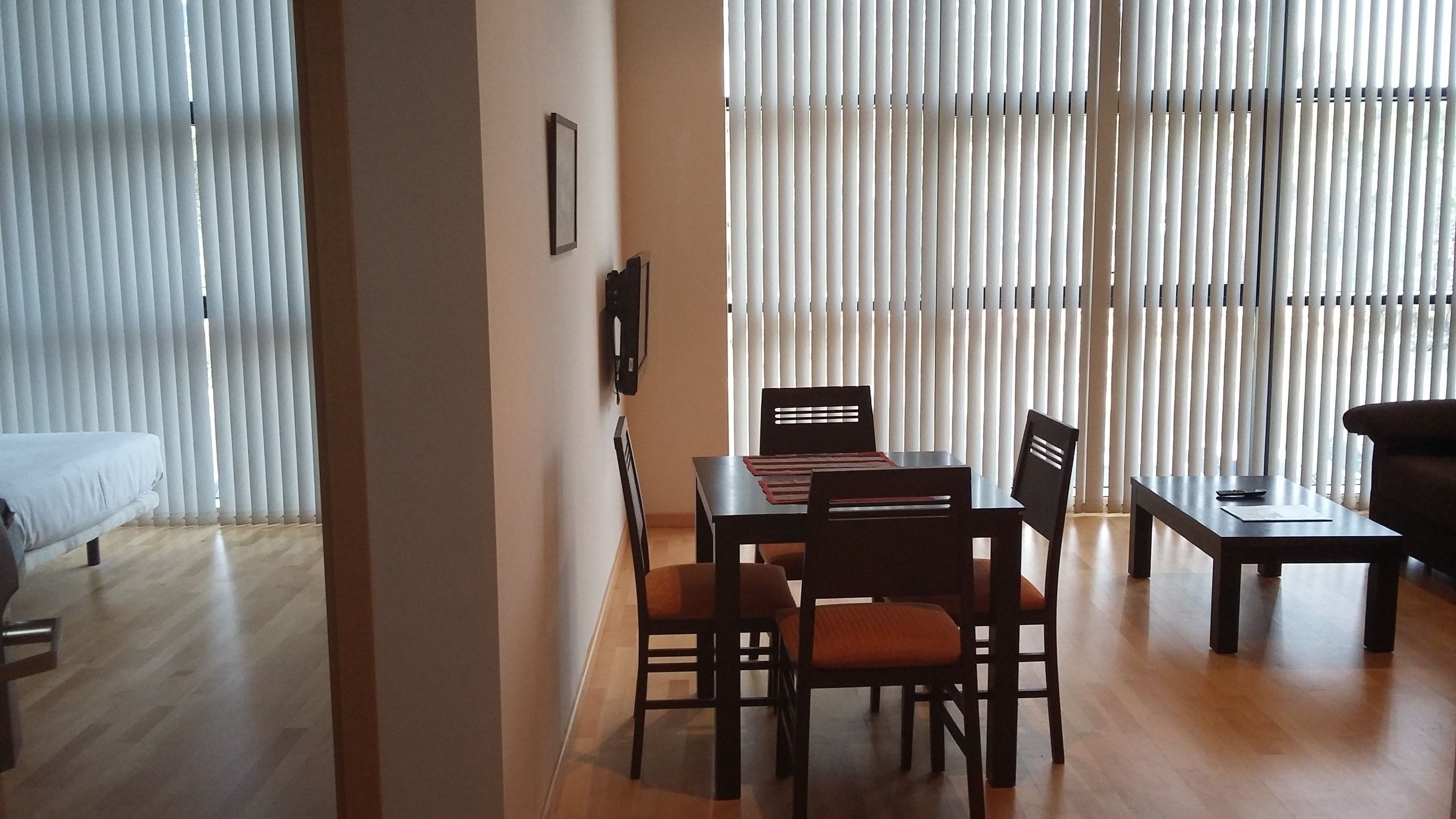 A dining area with a table and chairs, a sofa, and a TV on the wall.