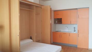 Un dormitorio con cama, un armario de madera y una kitchenette con armarios color naranja y un microondas.
