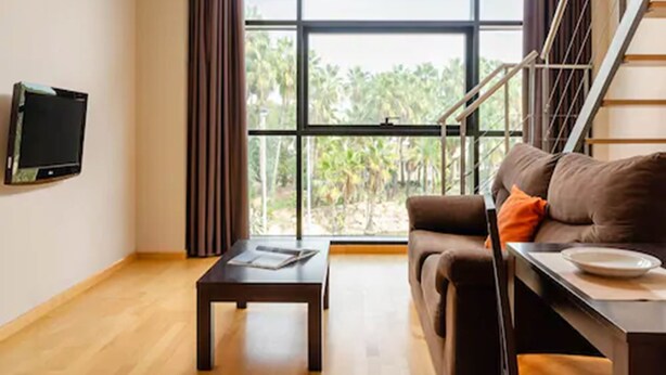 A modern living room with a large window, a sofa, a coffee table, and a TV mounted on the wall. - Aparthotel Wellness (Paterna)