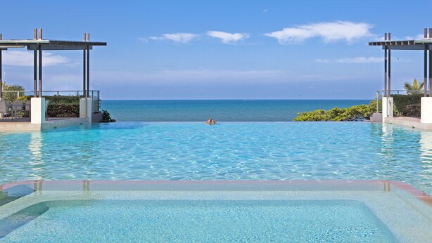 A clear blue pool with a view of the ocean, surrounded by a pergola and greenery. - Vue Apartments Trinity Beach (Trinity Beach)