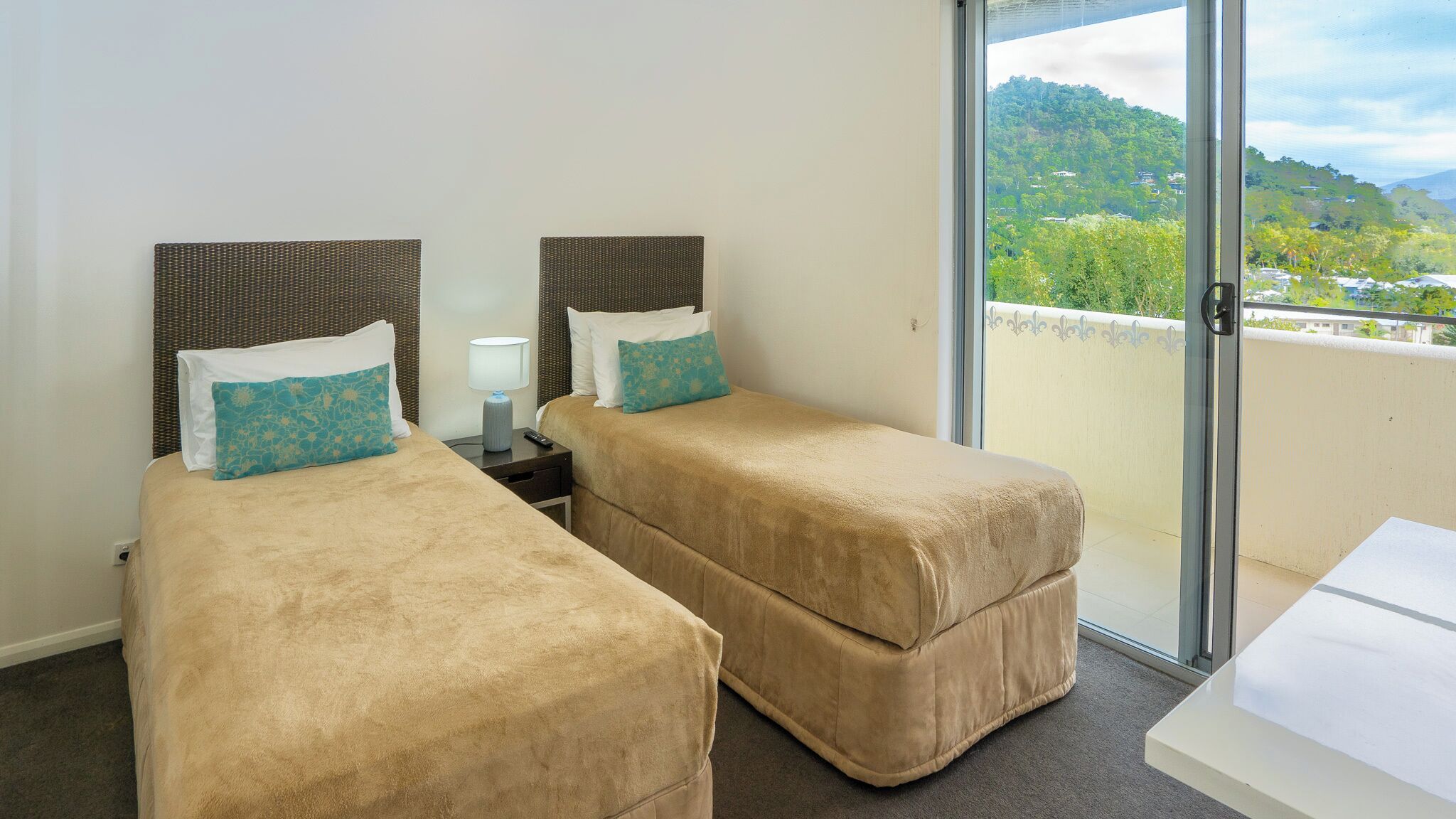 Ein Hotelzimmer mit zwei Einzelbetten, einem kleinen Tisch, einem Nachttisch und einem Balkon mit Blick auf eine grüne Hügellandschaft.