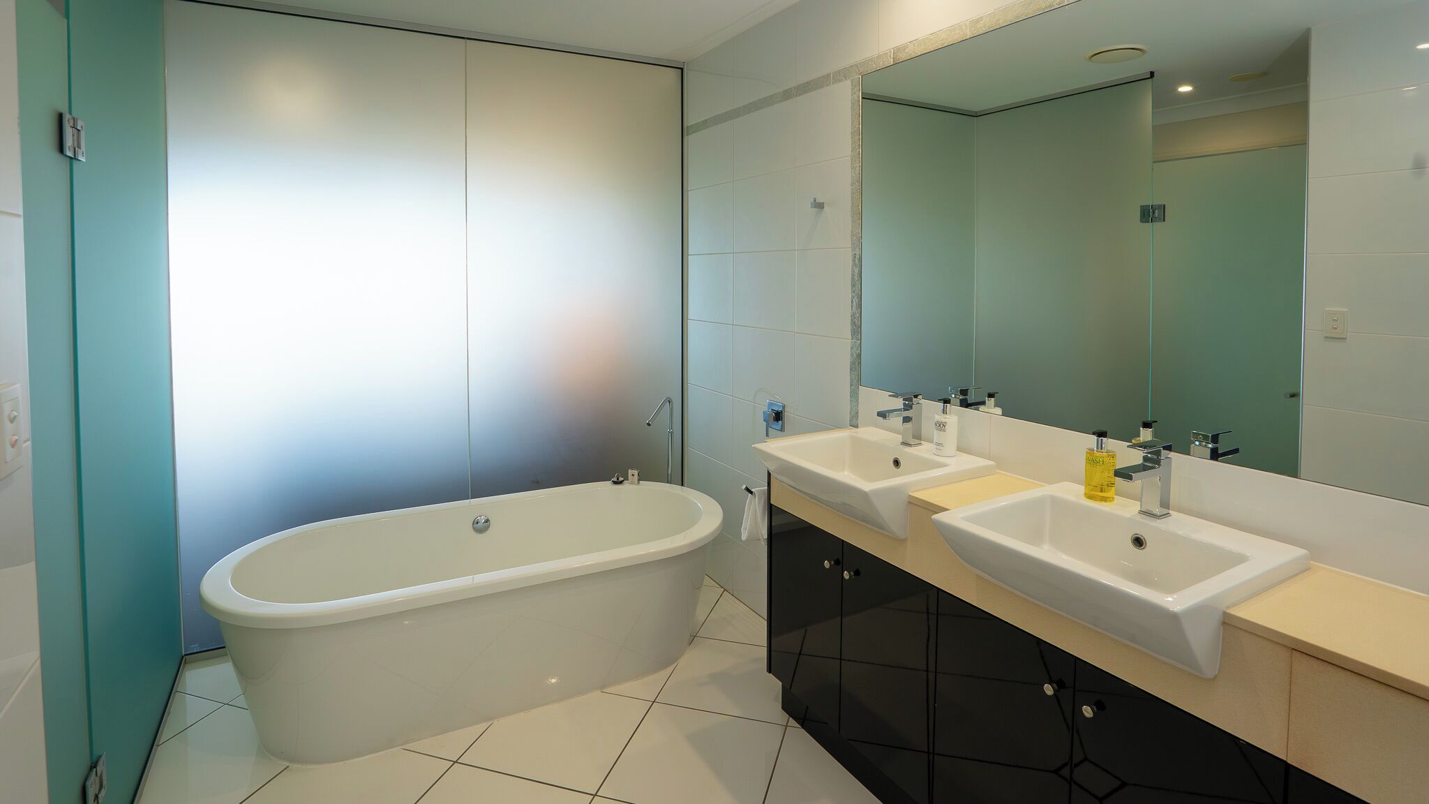 A modern bathroom with a freestanding bathtub, two sinks, and a large mirror.