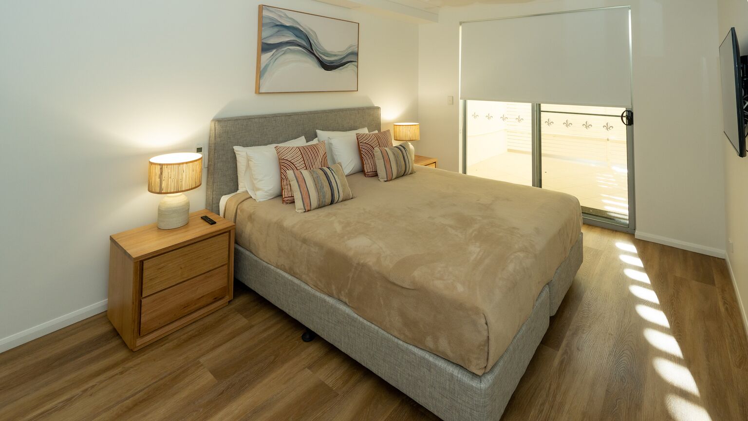 A bedroom with a bed, nightstands, a lamp, a painting, and a view through a window.