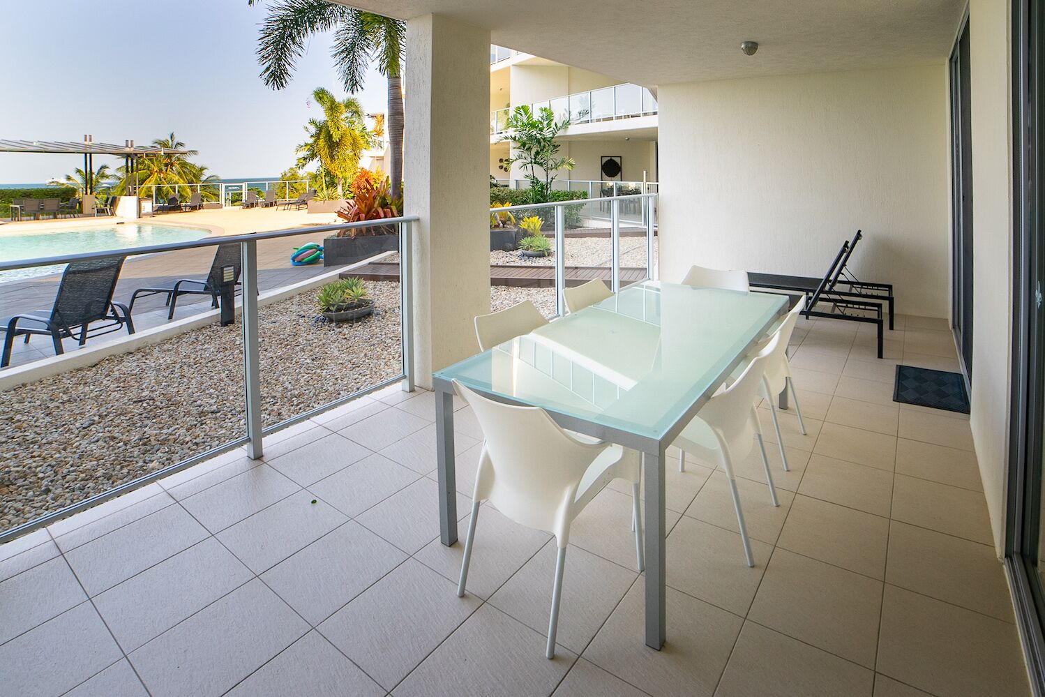 A modern outdoor area with a glass table and chairs, a pool, and a view of the ocean.