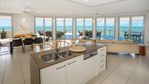 A modern kitchen with a large island, a dining area with chairs, and a sofa. - Vue Apartments Trinity Beach (Trinity Beach)