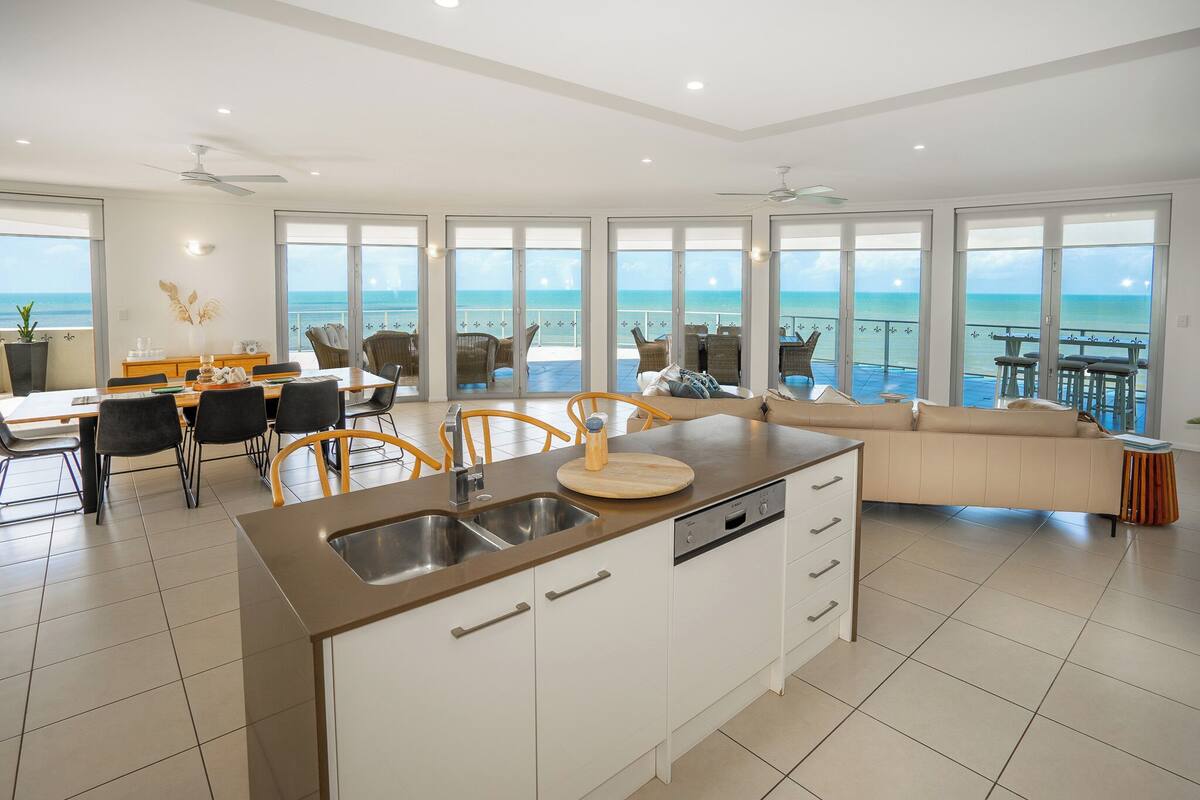 A modern kitchen with a large island, a dining area with chairs, and a sofa.