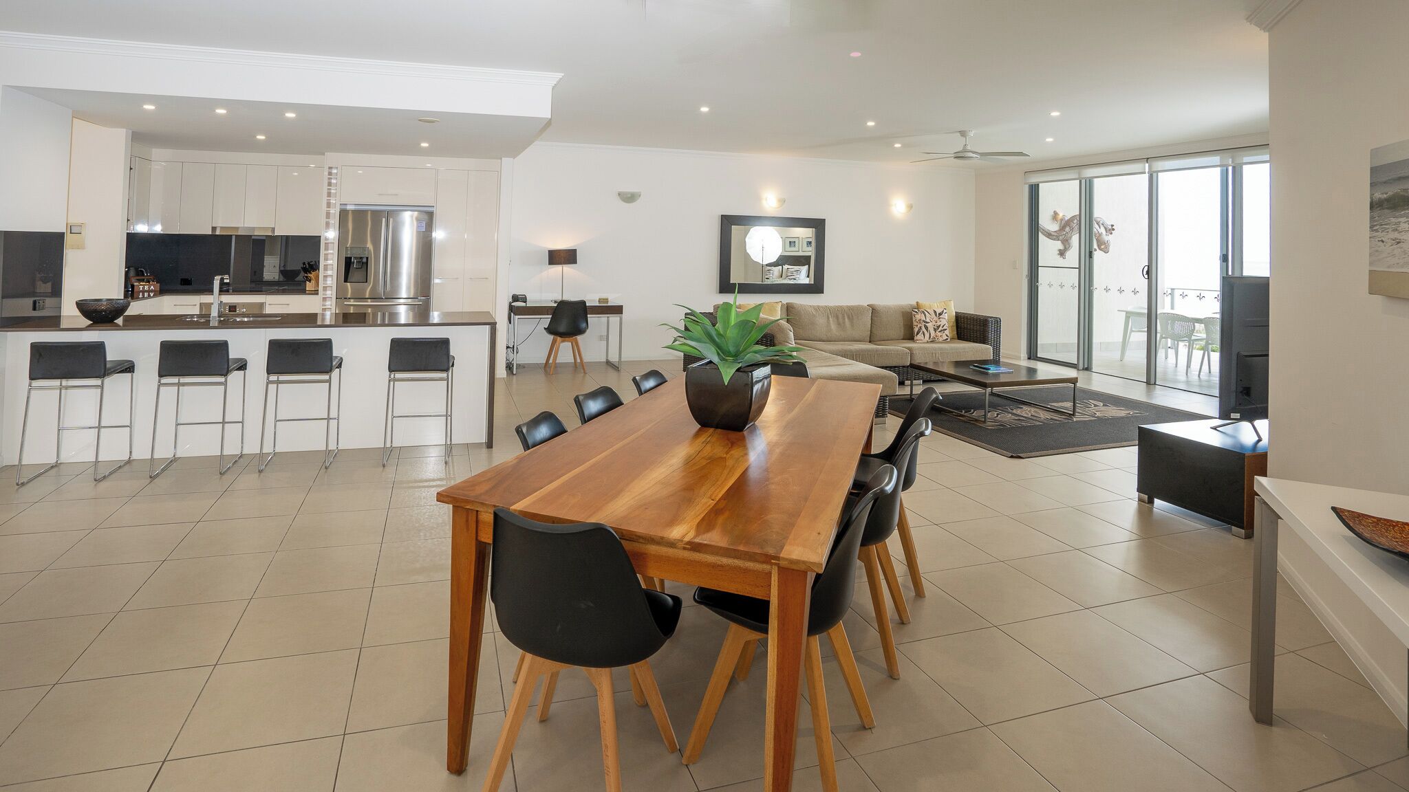 Une cuisine moderne avec des meubles blancs, un réfrigérateur en acier inoxydable et un coin repas comprenant une table en bois et des chaises noires.