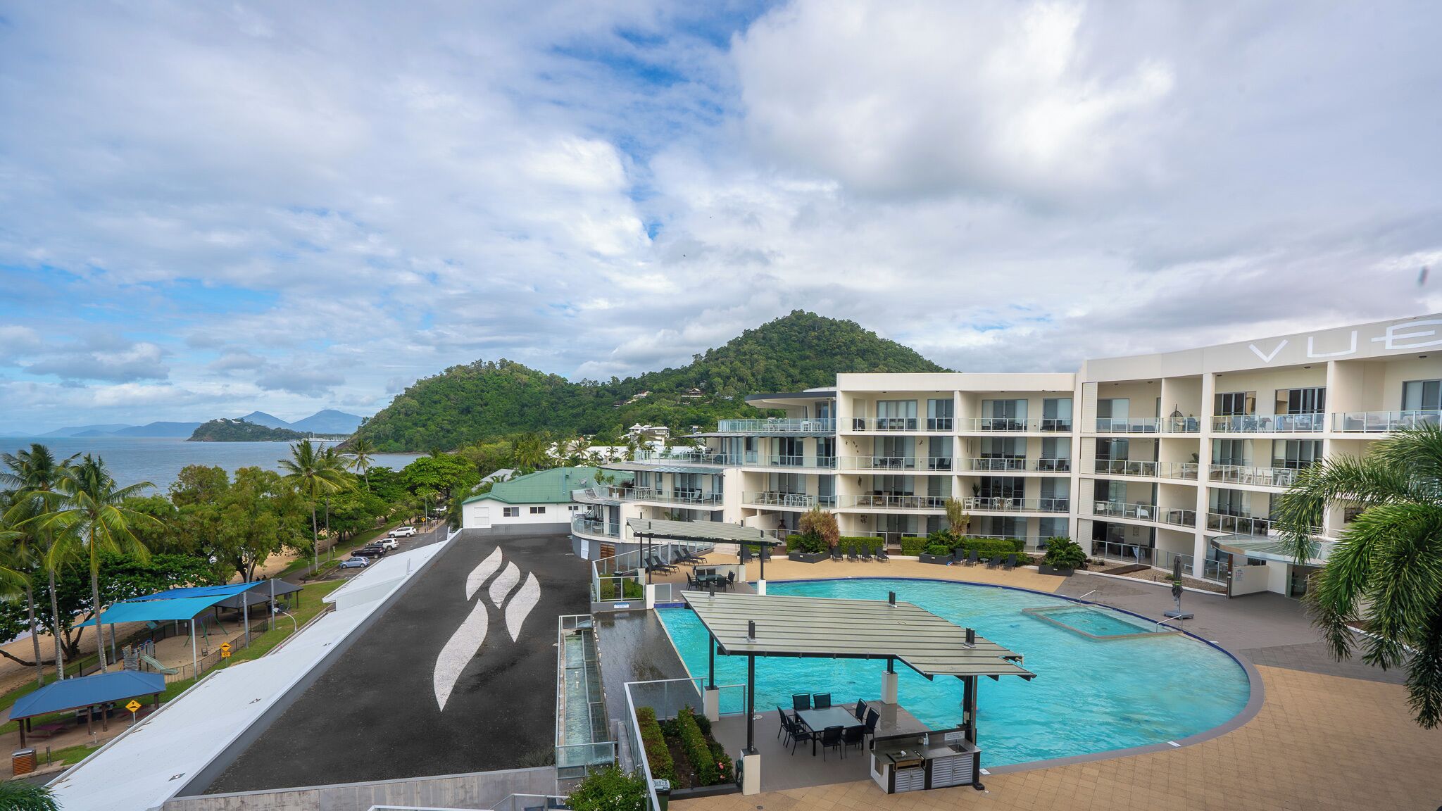 A hotel with a pool, outdoor seating, and a view of the sea and mountains.