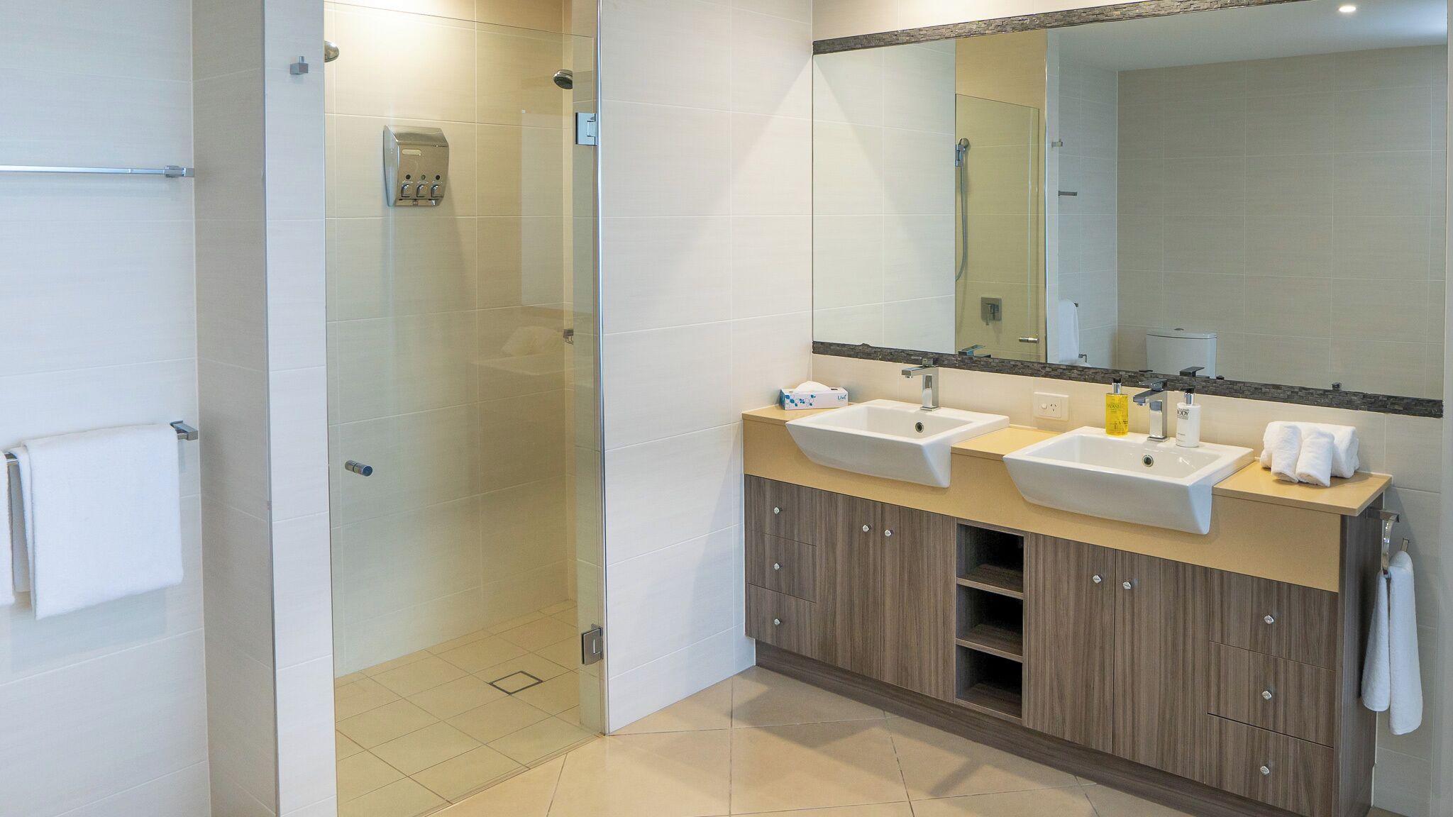 A modern bathroom with a glass-enclosed shower, two sinks, a large mirror, and wooden cabinets.