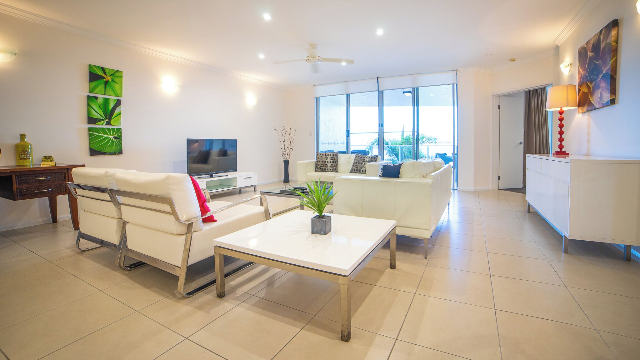 A modern living room with a sofa, a coffee table, a TV, and a balcony with a view.