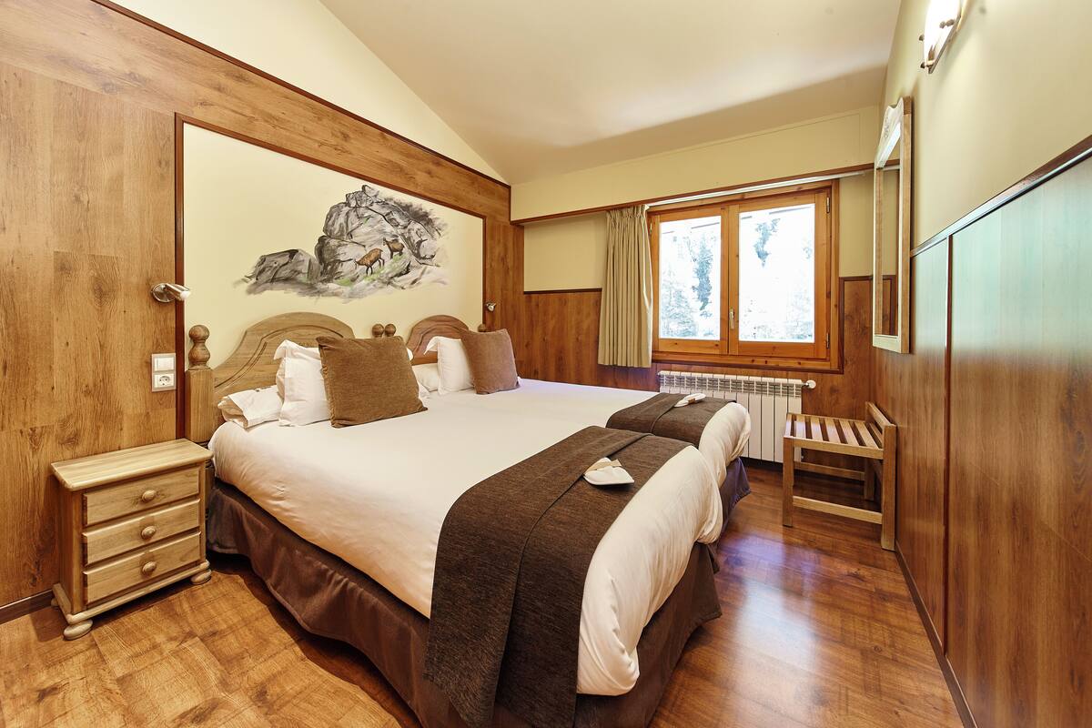 A double bed with a headboard, a nightstand, a bench, and a window with curtains.