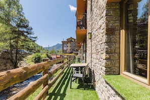 A stone building with a wooden deck and a table and chairs set up for outdoor dining. - Apartaments La Neu (Llorts)