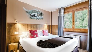 A hotel room with a large bed, wooden headboard, a painting of a snowy landscape, and a window with a view of trees. - Apartaments La Neu (Llorts)