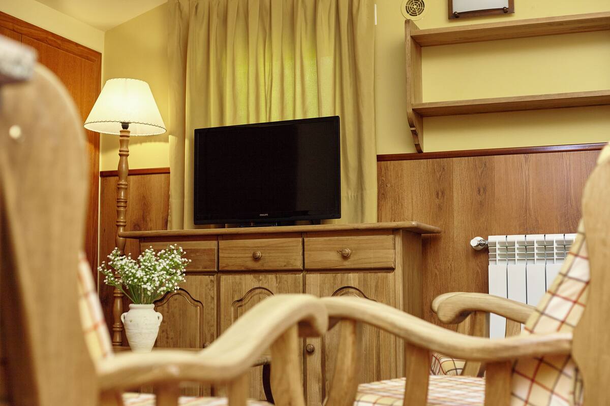 A wooden cabinet with a flat-screen TV, a lamp, and a vase with flowers.