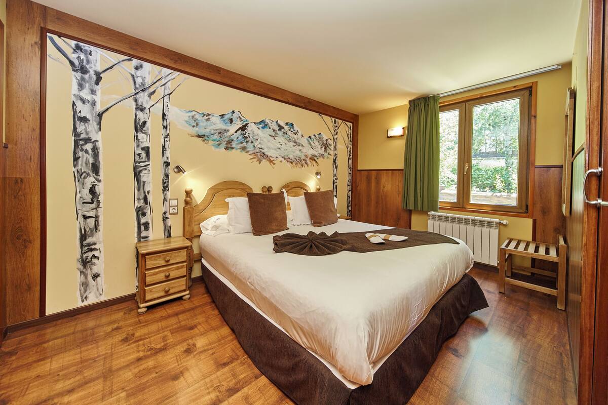 A bedroom with a large bed, wooden nightstands, a wall mural, and a window with curtains.