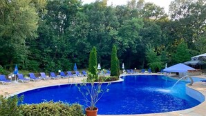A swimming pool with blue water, surrounded by lounge chairs and umbrellas, with trees in the background. - Boutique SPA Hotel Orchidea (Golden Sands)