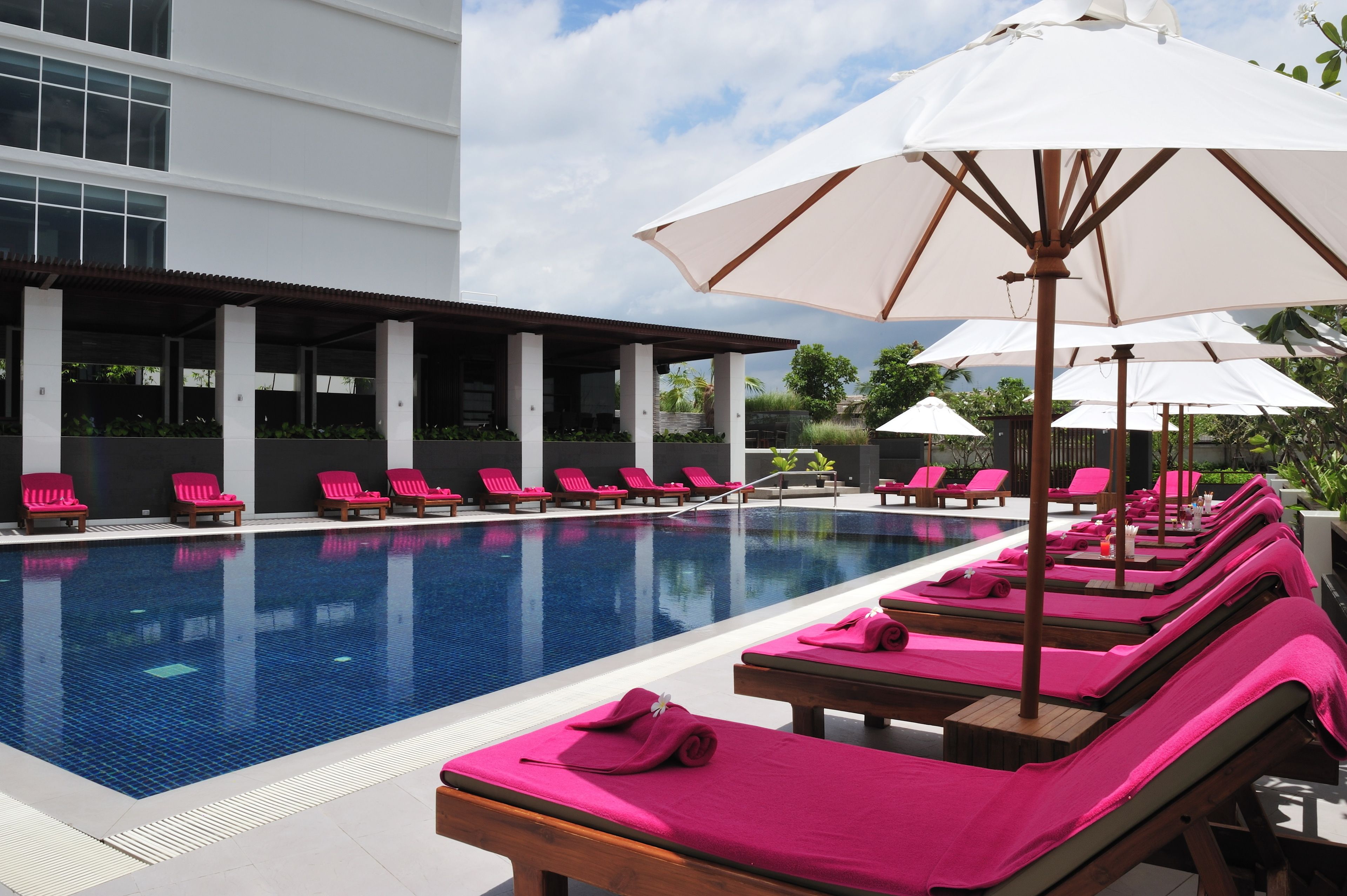A swimming pool with lounge chairs and umbrellas, surrounded by a modern building with large windows.