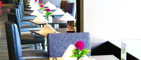 A restaurant with tables set for dining, featuring a menu stand and a flower centerpiece.