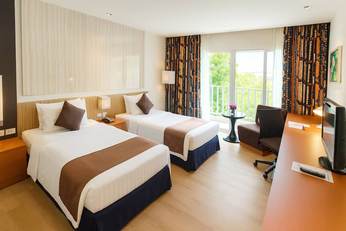 Ein Hotelzimmer mit zwei Betten, einem Schreibtisch, einem Fernseher und einem Balkon mit Vorhängen.
