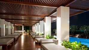 A covered outdoor lounge area with wooden flooring, cushioned seating, and a pool view. - Amaranth Suvarnabhumi Hotel - Free Suvarnabhumi Airport Shuttle (Bang Phli)