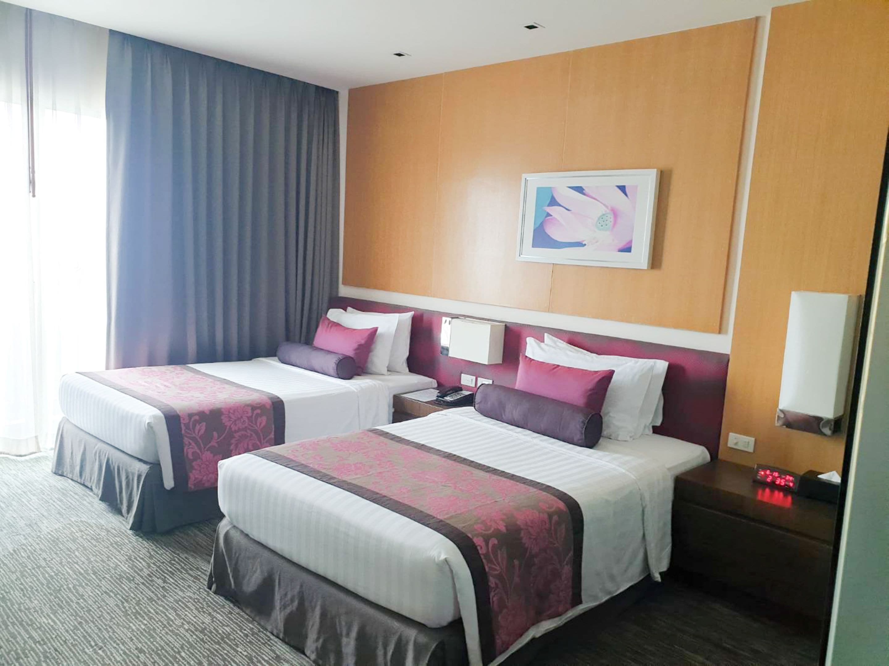 Ein Hotelzimmer mit zwei Betten, einem Holz-Kopfteil, einem Gemälde, einem Nachttisch und einer Uhr.