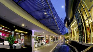 A modern hotel corridor with glass walls, a reflective pool, and a blue ceiling. - Amaranth Suvarnabhumi Hotel - Free Suvarnabhumi Airport Shuttle (Bang Phli)