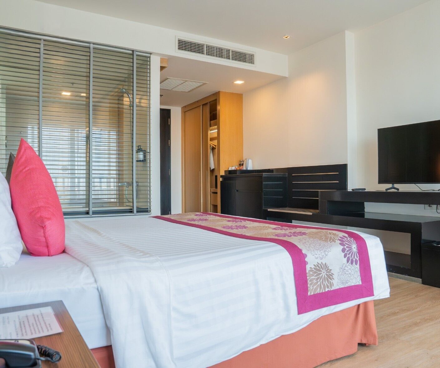 A hotel room with a bed, a desk with a computer, a TV, and a wardrobe.