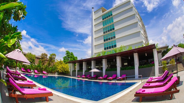 A swimming pool with lounge chairs and umbrellas, surrounded by a building with a modern design and a clear blue sky. - Amaranth Suvarnabhumi Hotel - Free Suvarnabhumi Airport Shuttle (Bang Phli)