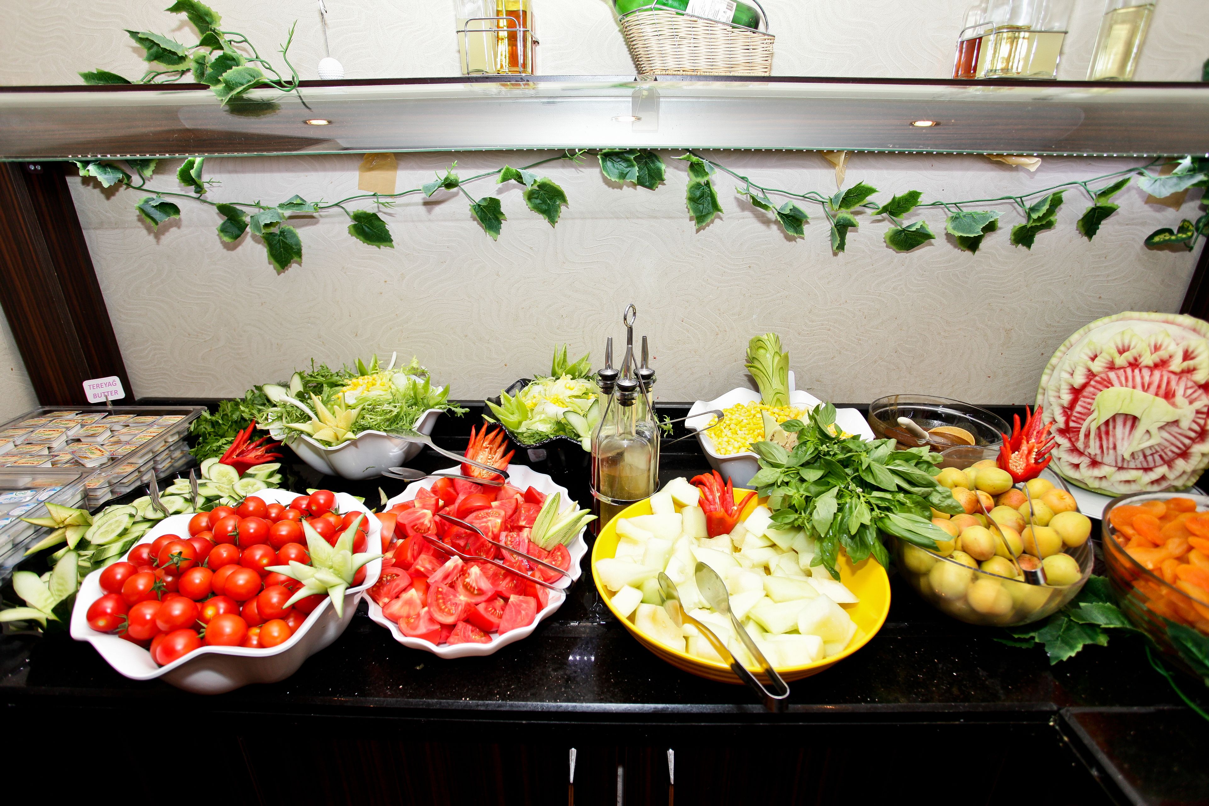 A buffet table with various food items including tomatoes, cucumbers, and leafy greens.
