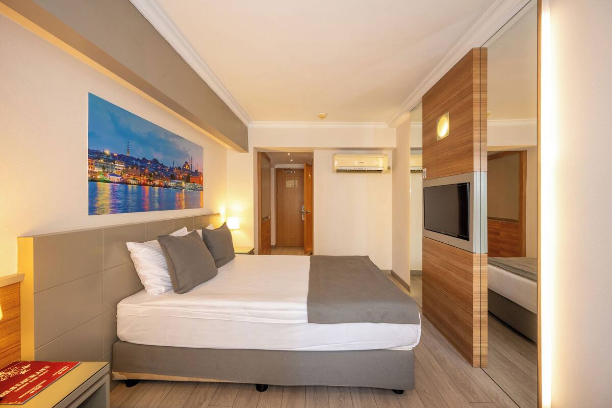 A hotel room with a large bed, a TV, and a painting of a cityscape.