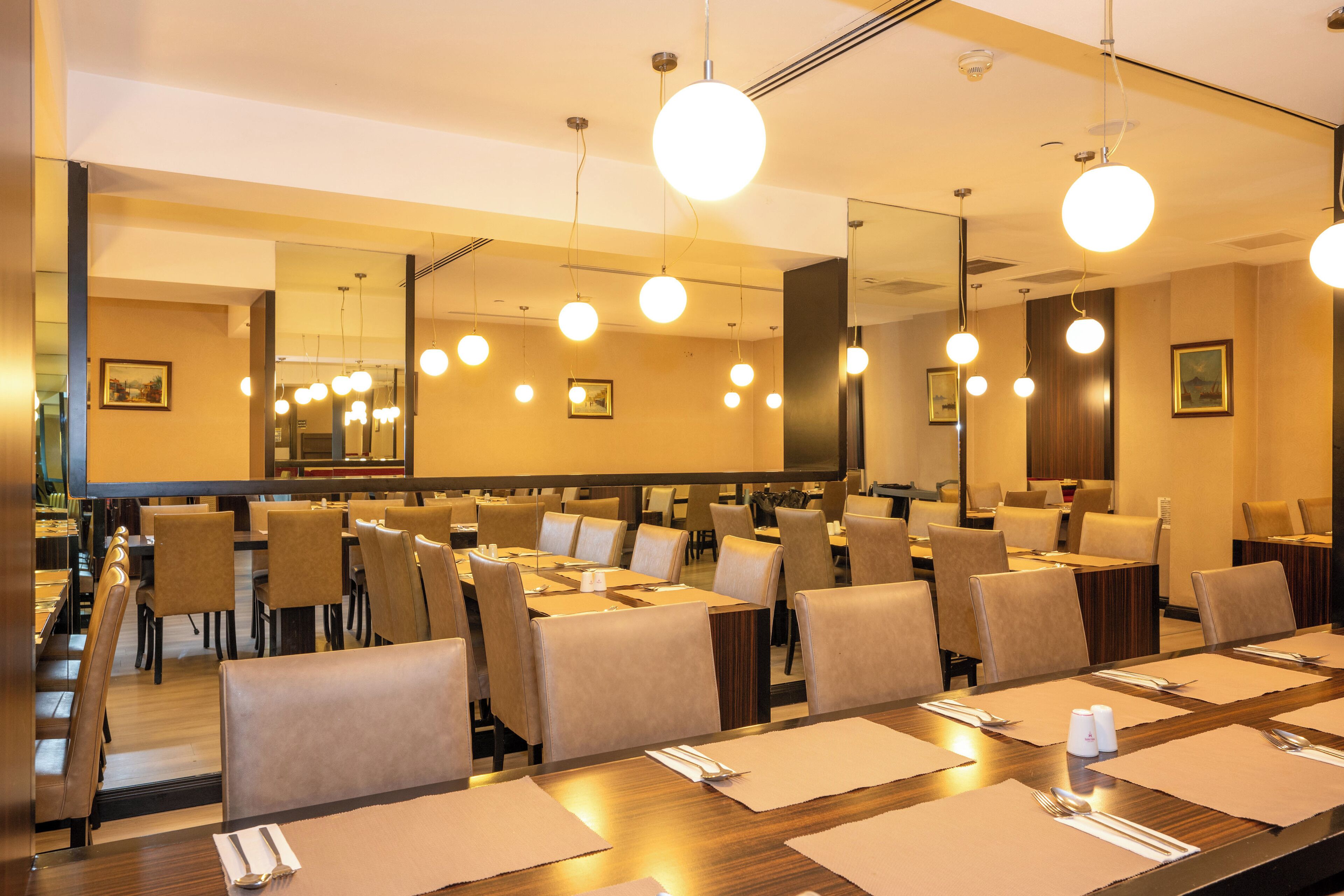 A hotel dining area with multiple tables set for dining, chairs, and hanging spherical lights.
