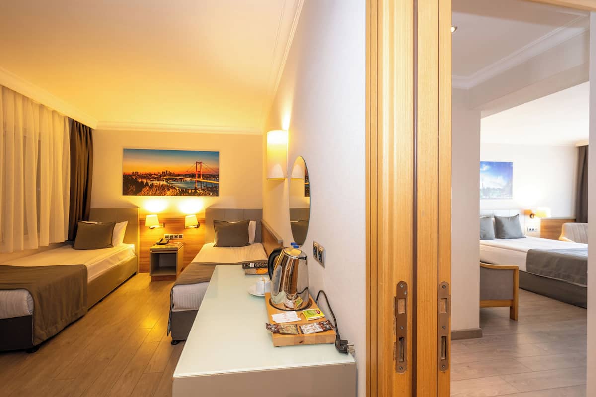 A hotel room with a bed, a sofa, a desk with a coffee maker, and a painting of a sunset on the wall.