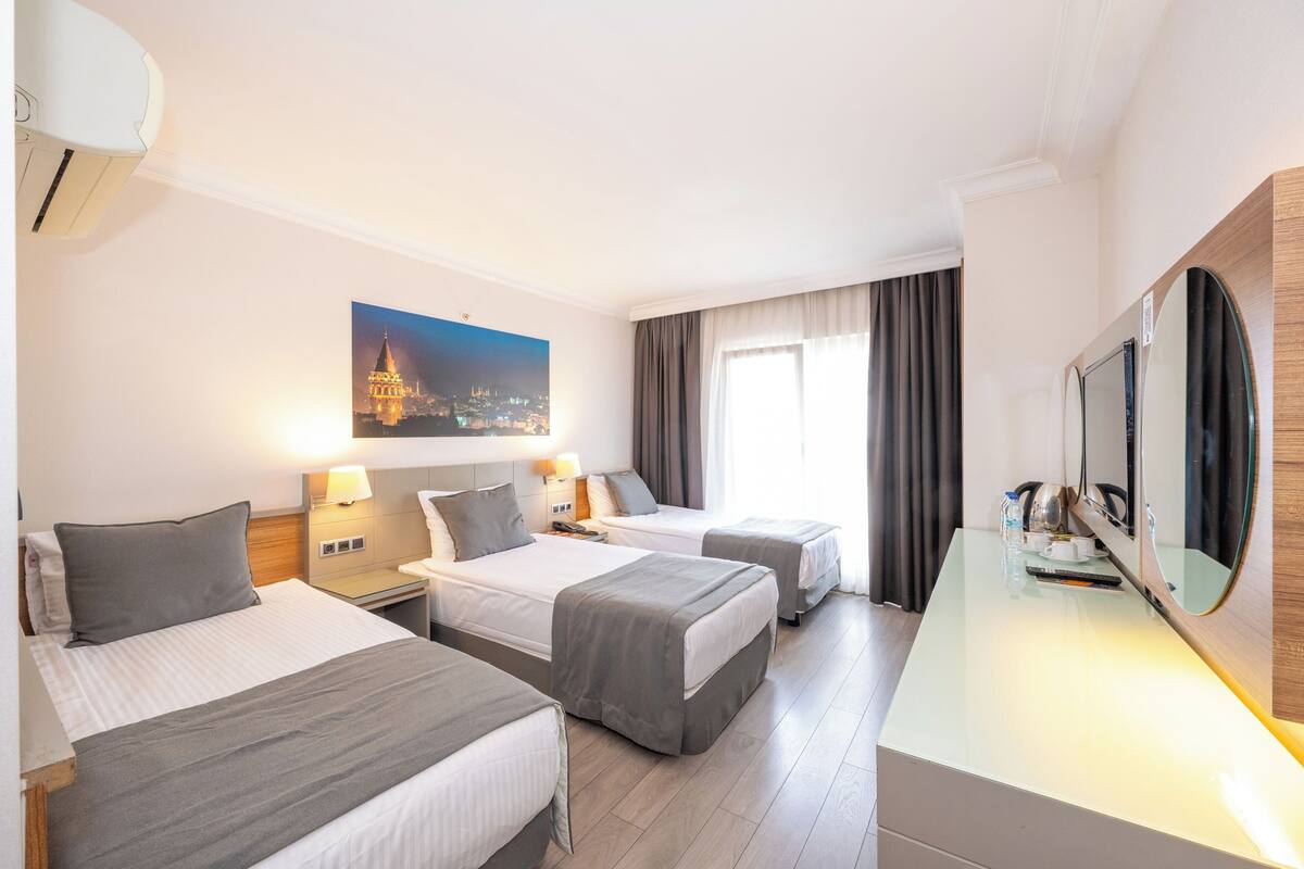 A hotel room with two beds, a desk, a large mirror, and a painting of a cityscape.