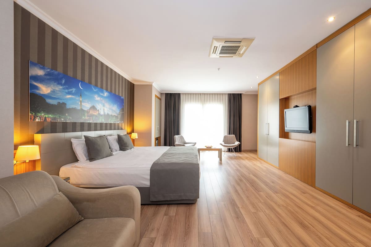 A modern hotel room with a large bed, a sofa, a TV, and a painting on the wall.