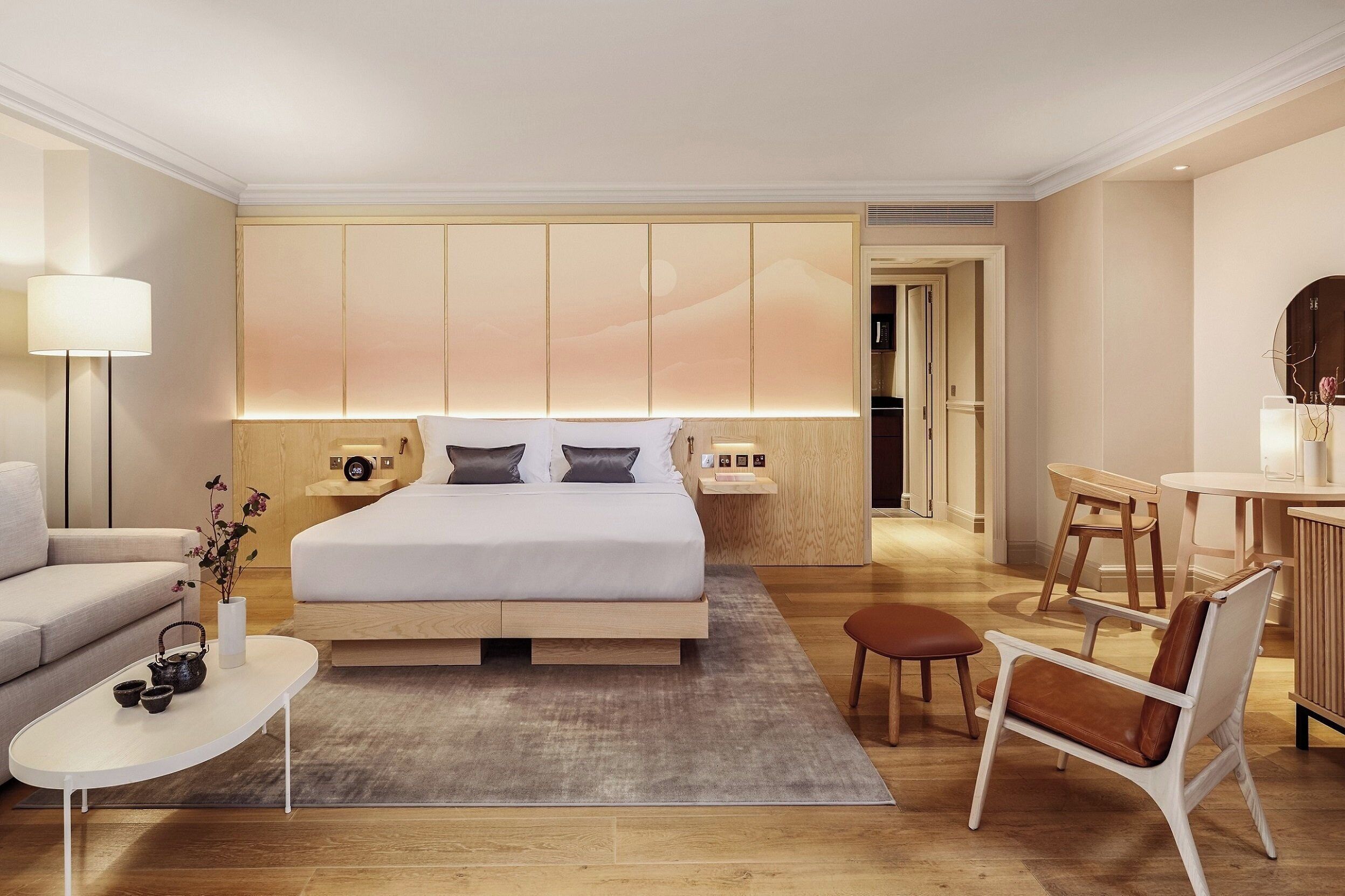 A modern hotel room with a large bed, bedside tables, a sofa, a small table with a vase, and a chair.