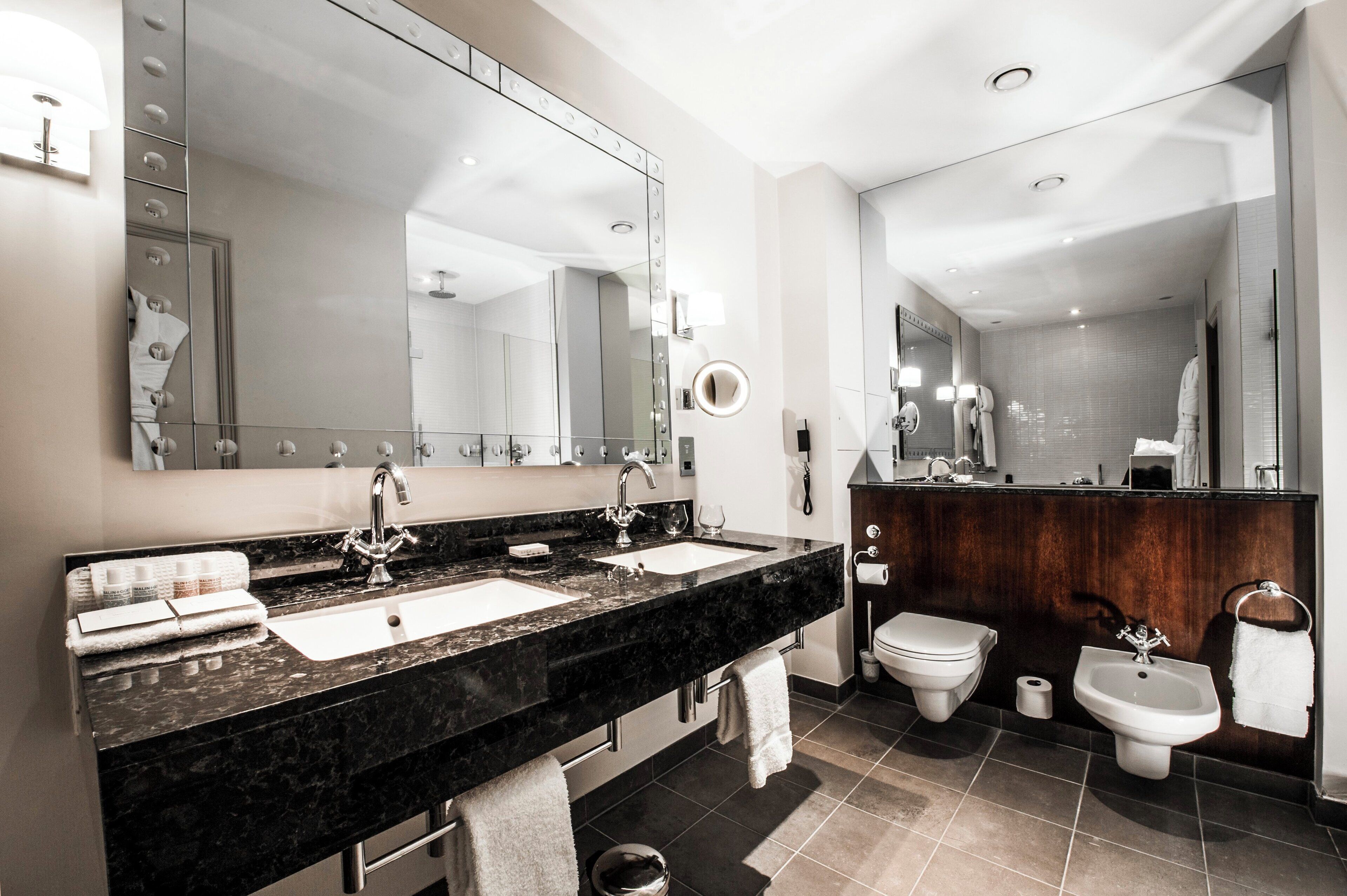 A modern bathroom with two sinks, a large mirror, a toilet, and a bidet.