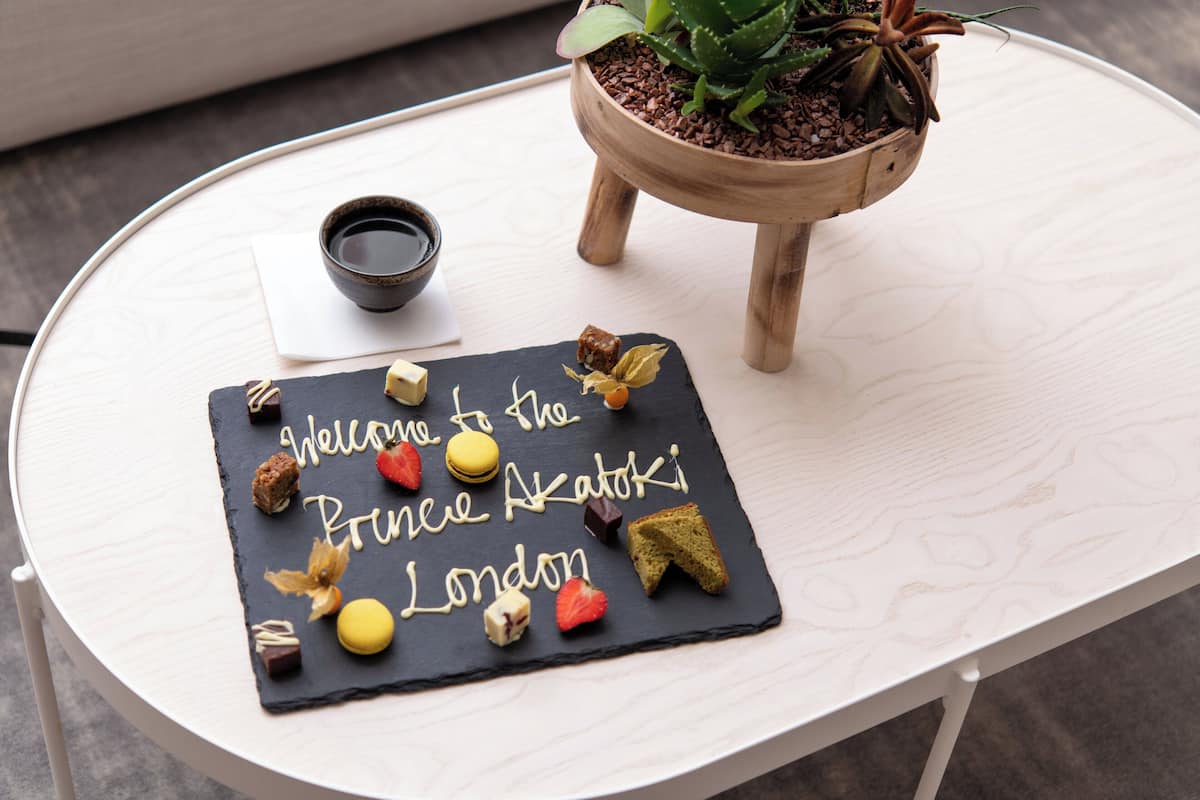 A welcome sign with a cake and snacks on a table, a small plant, and a cup of tea.