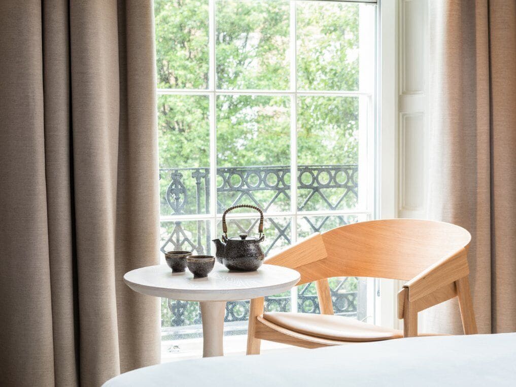 A room with a table and chair near a window with a view of greenery.