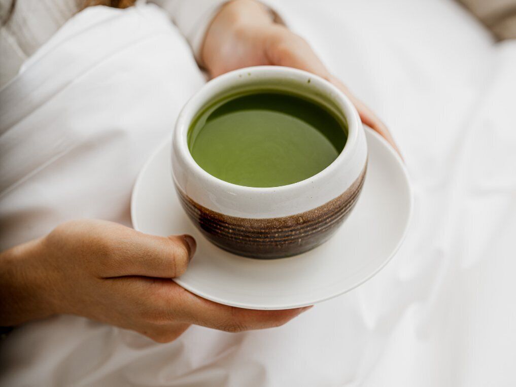 Une personne tenant une tasse de thé vert sur une assiette blanche.